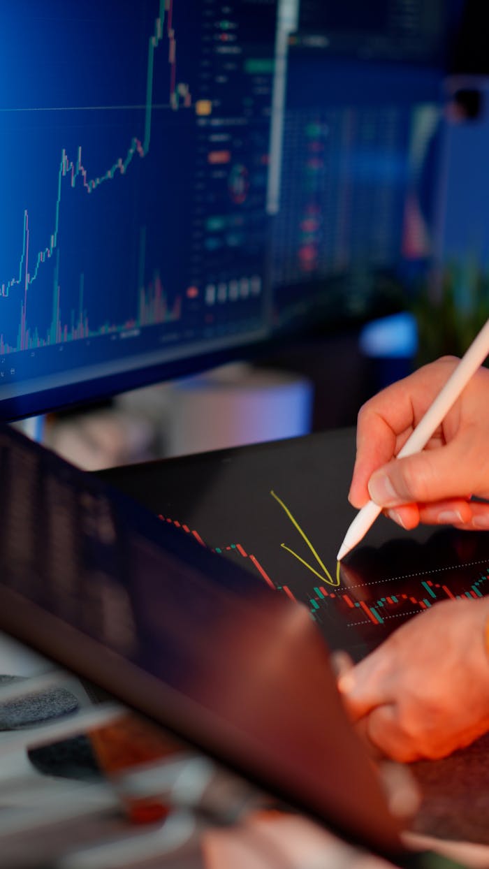 hero-img-01 Person using a stylus on a tablet for stock market analysis, with charts on a monitor.